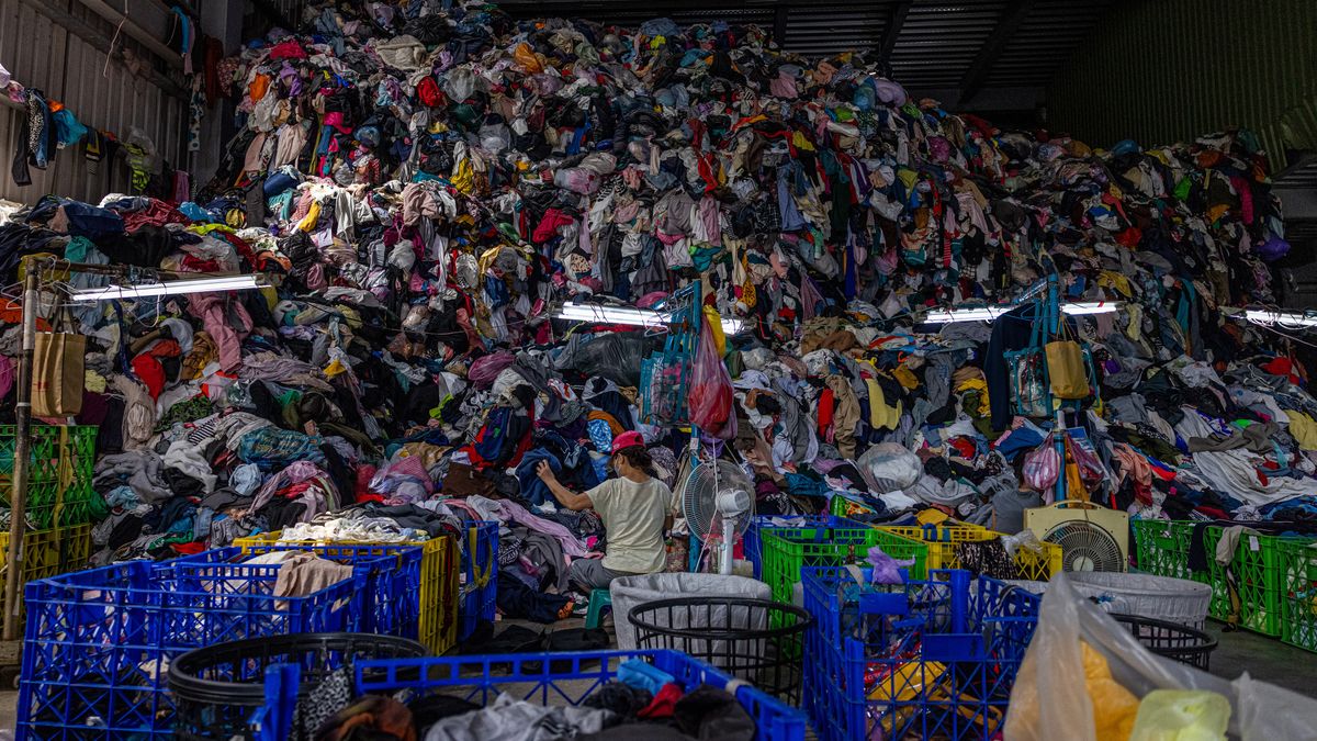 A person is seen sorting through fabrics next to a giant pile of textile waste ready for recycling.