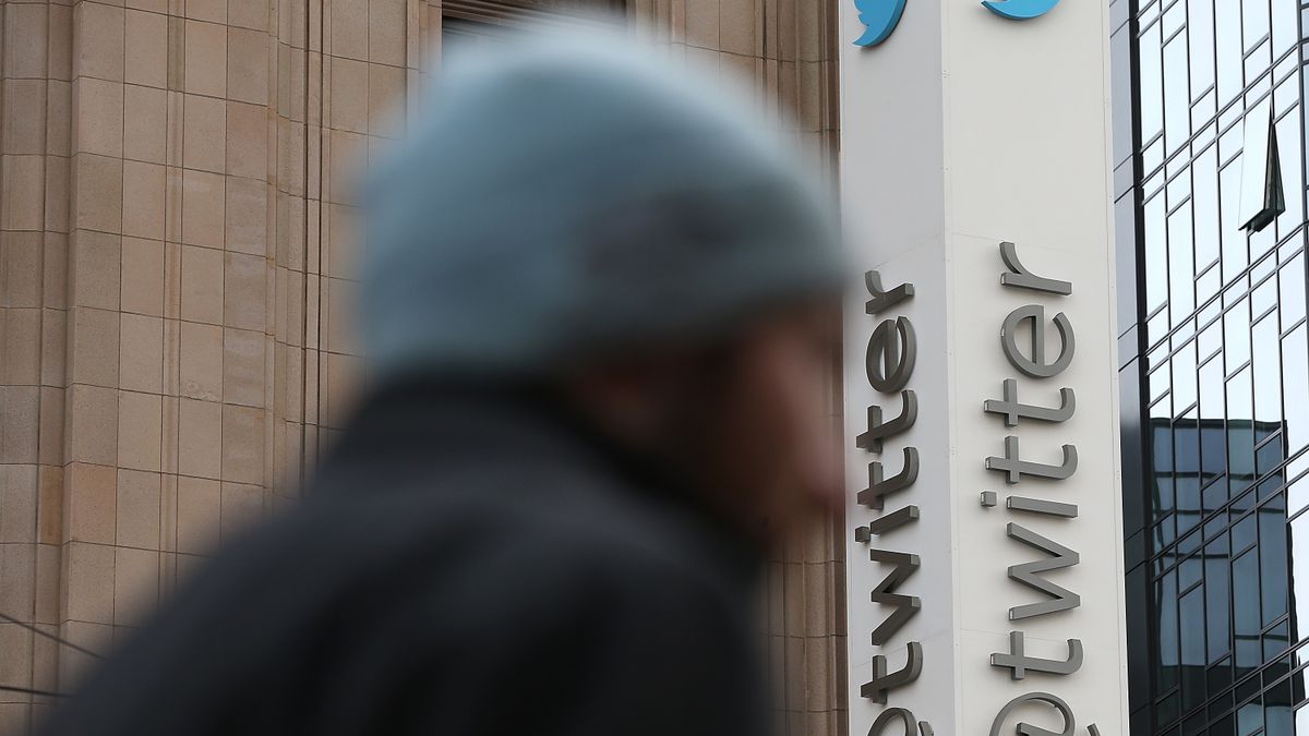 Medium shot of Twitter headquarters' @twitter sign; a person, blurred, passes in front of the camera