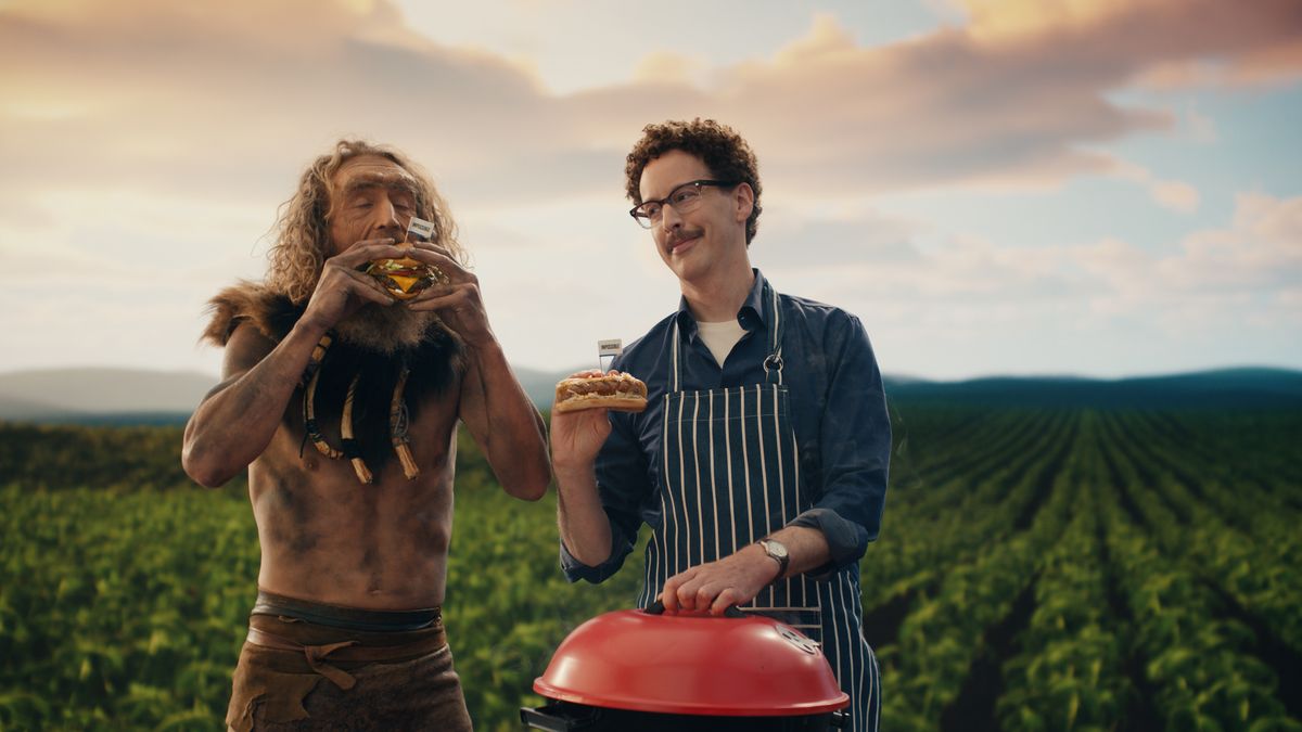 Two people, one dressed as a caveman and the other manning a grill, enjoy Impossible Burgers.