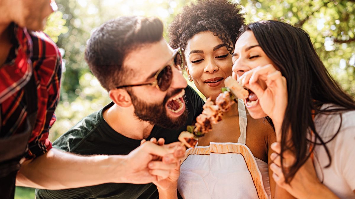 Friends at a cookout eating off a skewer