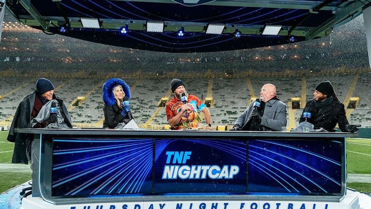 A panel of five "Thursday Night Football" presenters host a show on the field in the snow.